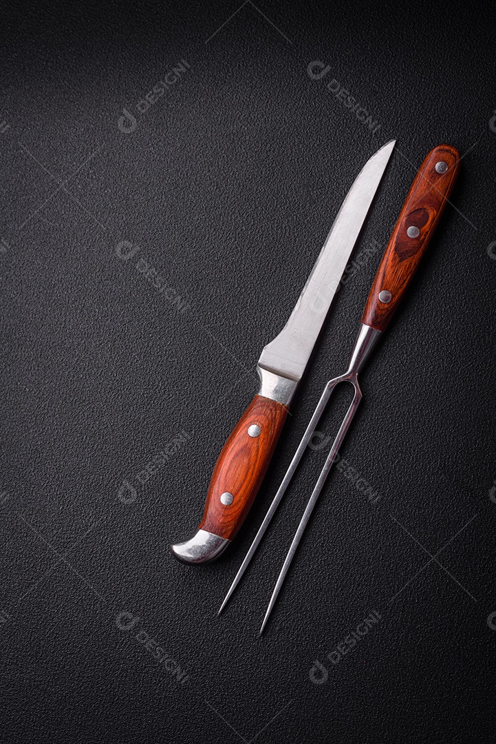 Faca e garfo de cozinha feitos de aço em um fundo escuro de concreto