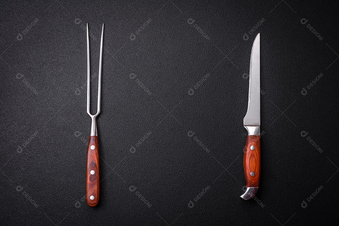 Faca e garfo de cozinha feitos de aço em um fundo escuro de concreto