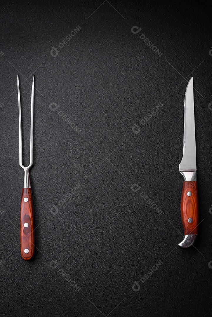 Faca e garfo de cozinha feitos de aço em um fundo escuro de concreto