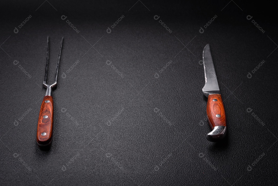 Faca e garfo de cozinha feitos de aço em um fundo escuro de concreto