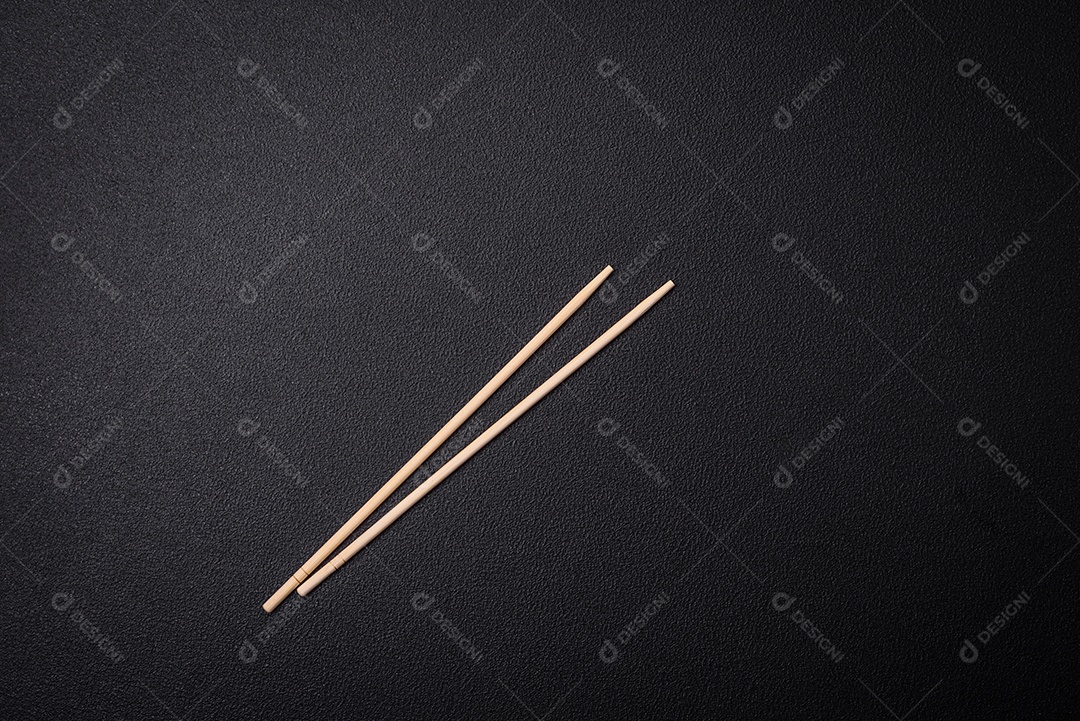 Pauzinhos de madeira brancos para pratos asiáticos em um fundo escuro de concreto