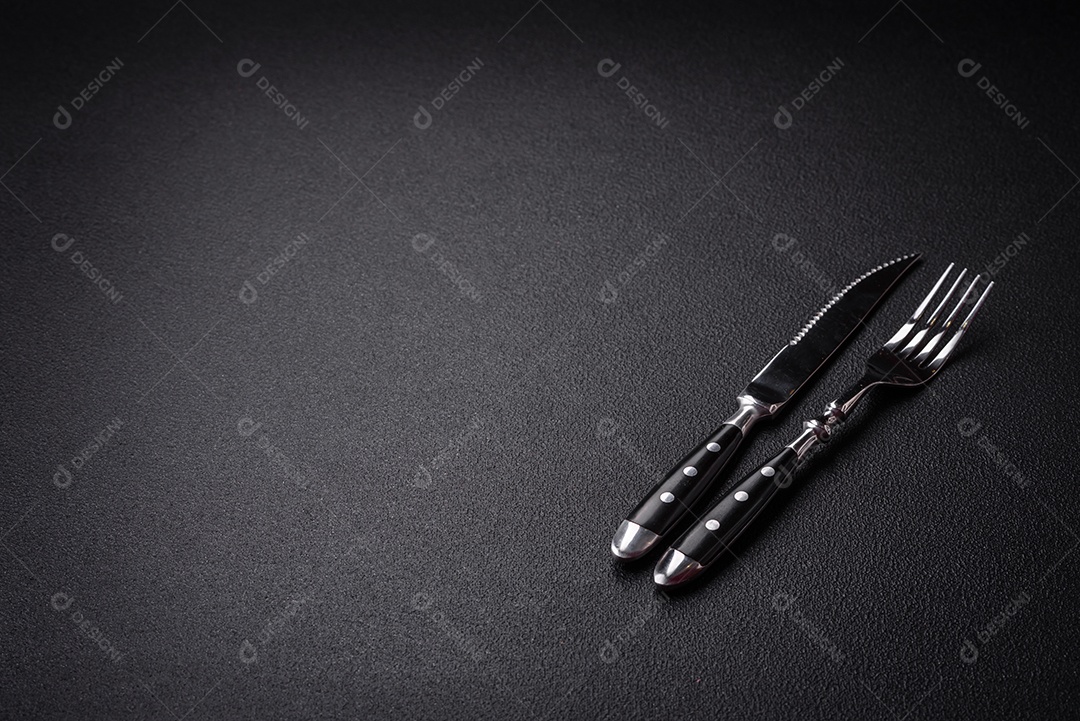 Faca e garfo de cozinha feitos de aço em um fundo escuro de concreto