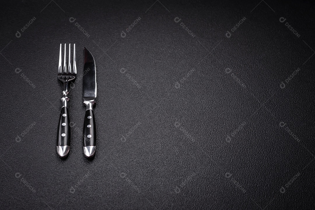 Faca e garfo de cozinha feitos de aço em um fundo escuro de concreto