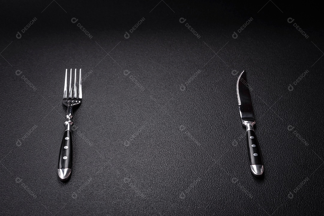 Faca e garfo de cozinha feitos de aço em um fundo escuro de concreto