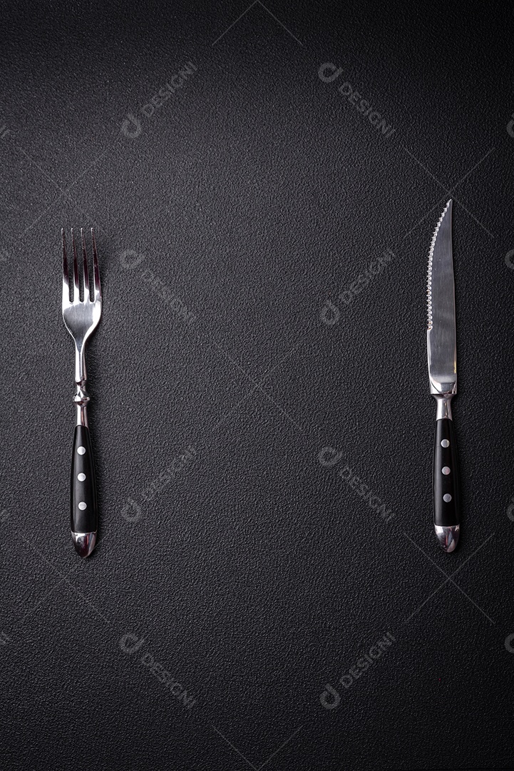 Faca e garfo de cozinha feitos de aço em um fundo escuro de concreto