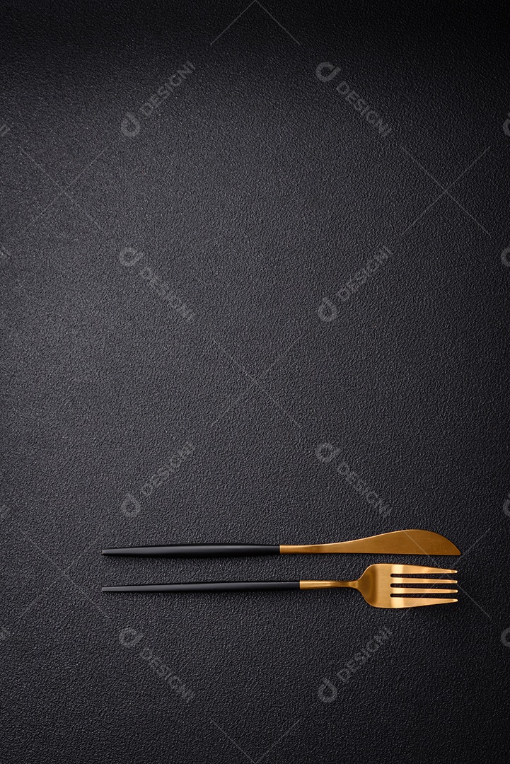 Faca e garfo de cozinha feitos de aço em um fundo escuro de concreto