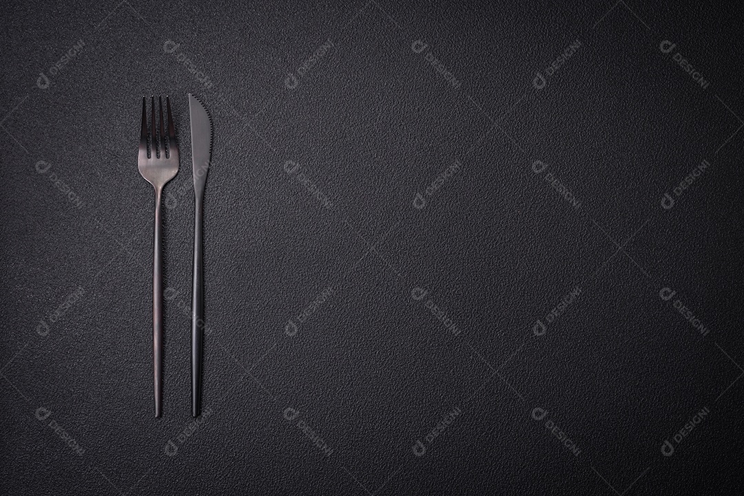 Faca e garfo de cozinha feitos de aço em um fundo escuro de concreto