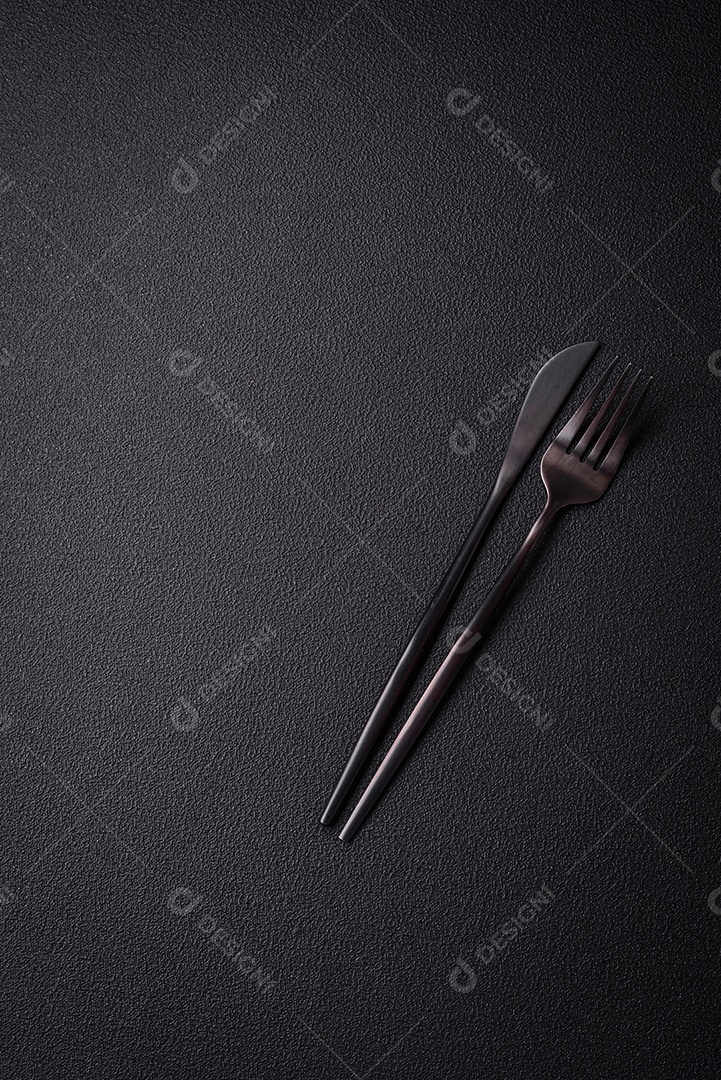 Faca e garfo de cozinha feitos de aço em um fundo escuro de concreto