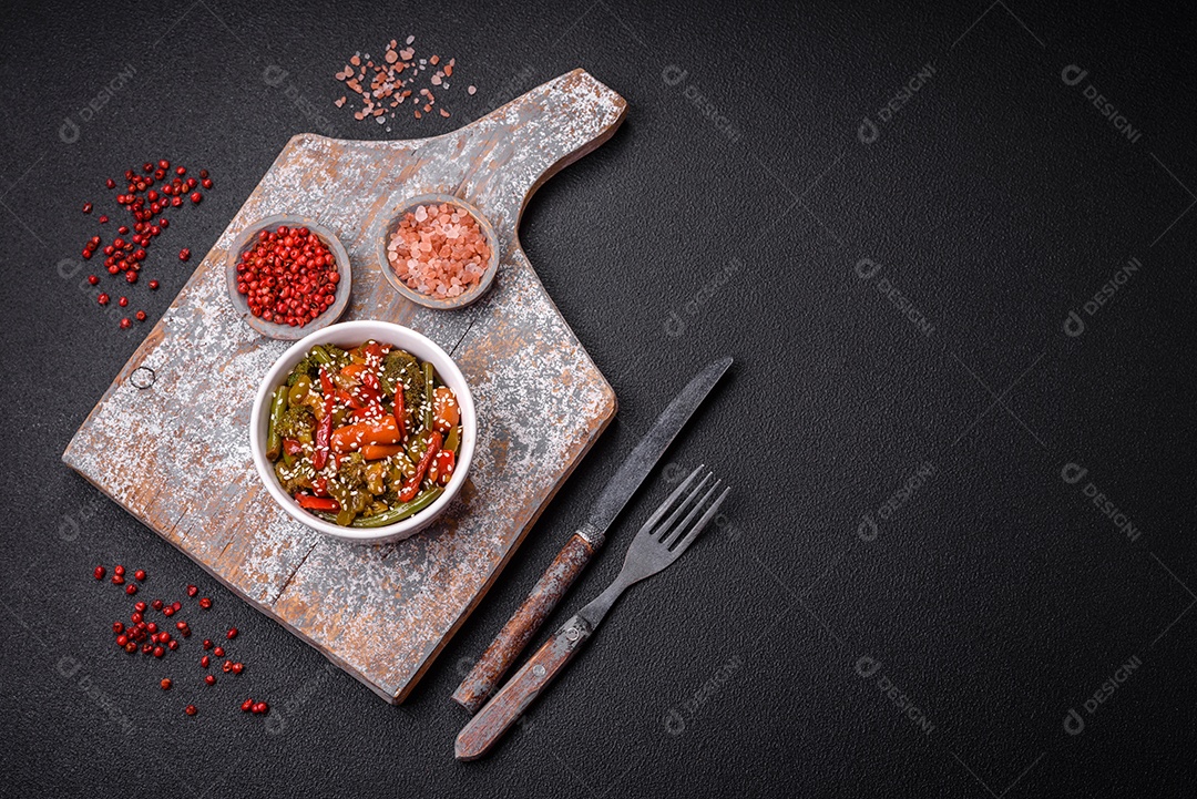 Mistura de legumes, milho, cenoura, pimentão, brócolis, cebola em molho teriyaki em uma placa de cerâmica sobre um fundo escuro de concret