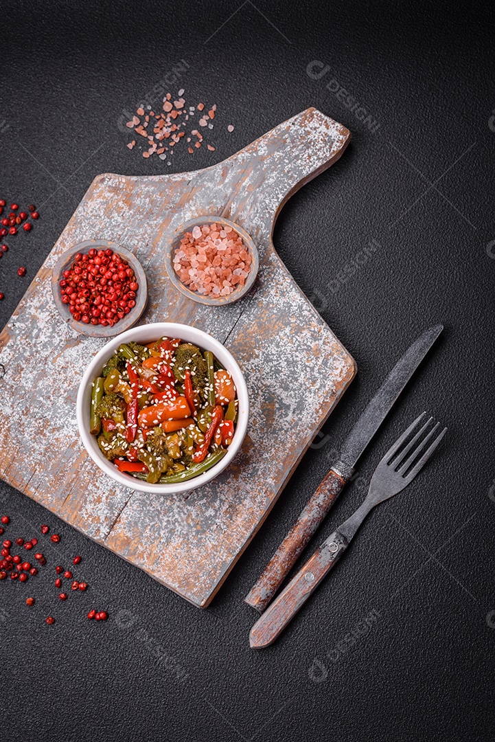 Mistura de legumes, milho, cenoura, pimentão, brócolis, cebola em molho teriyaki em uma placa de cerâmica sobre um fundo escuro de concreto