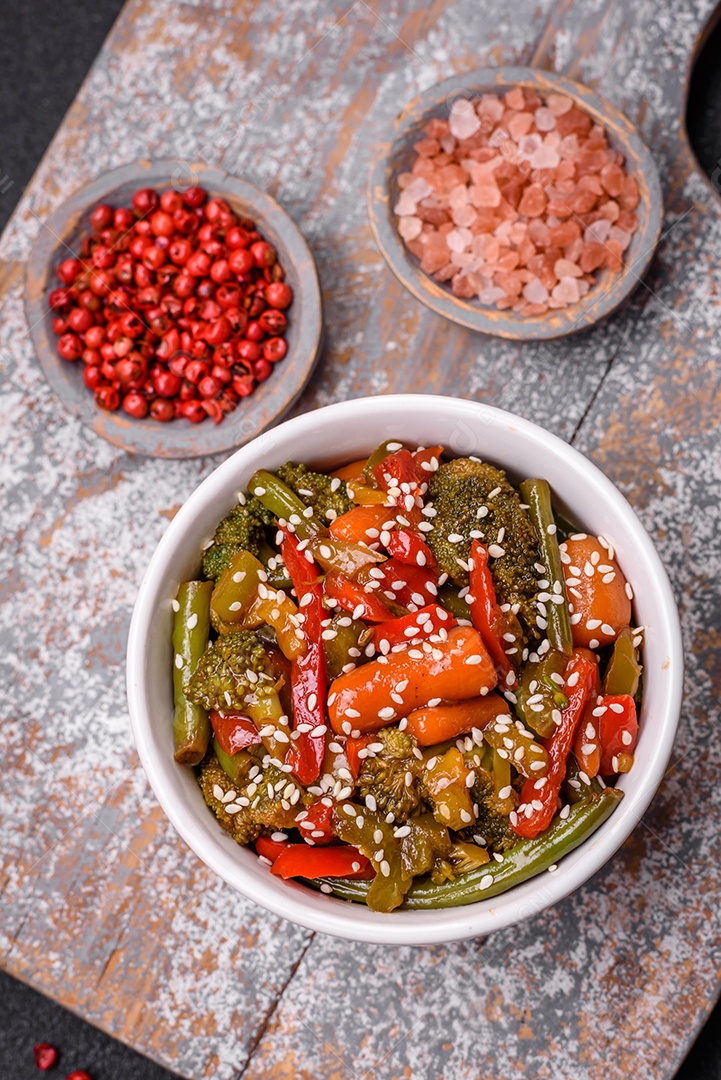 Mistura de legumes, milho, cenoura, pimentão, brócolis, cebola em molho teriyaki em uma placa de cerâmica sobre um fundo escuro de concreto