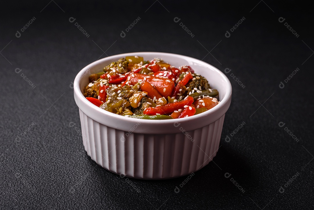 Mistura de legumes, milho, cenoura, pimentão, brócolis, cebola em molho teriyaki em uma placa de cerâmica sobre um fundo escuro de concreto