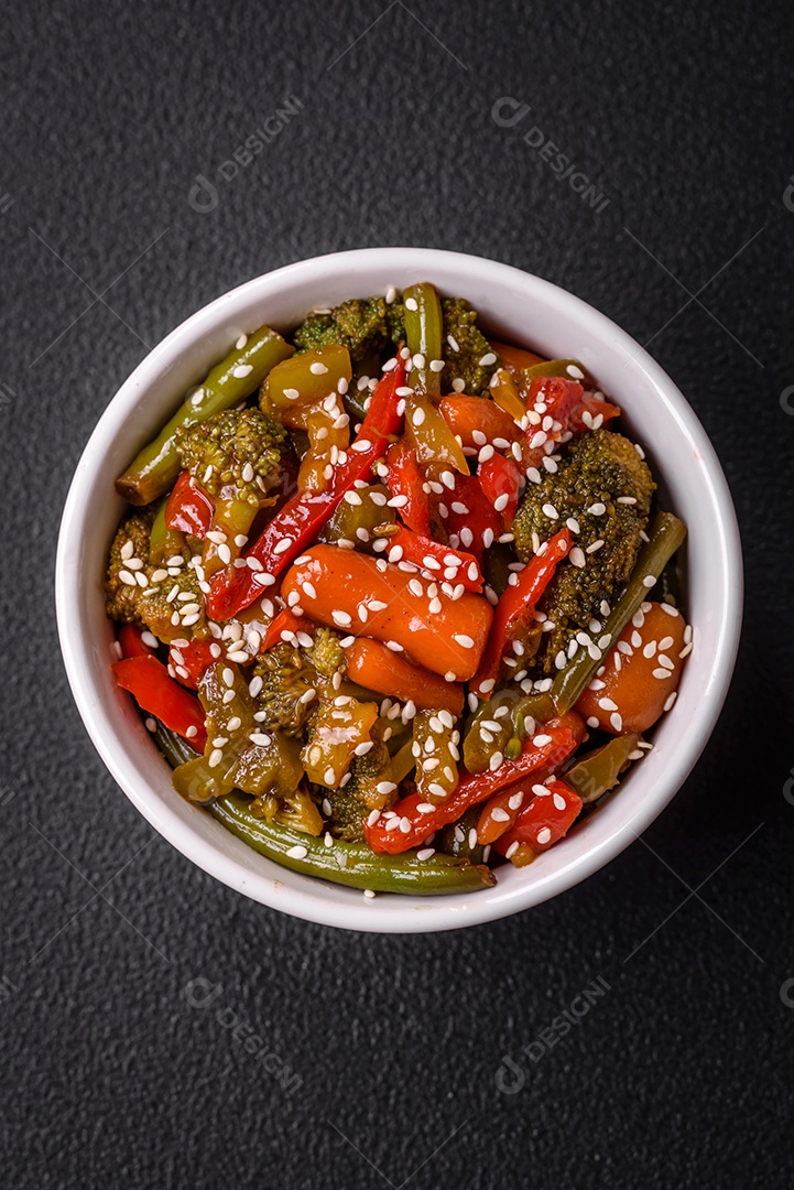 Mistura de legumes, milho, cenoura, pimentão, brócolis, cebola em molho teriyaki em uma placa de cerâmica sobre um fundo escuro de concreto