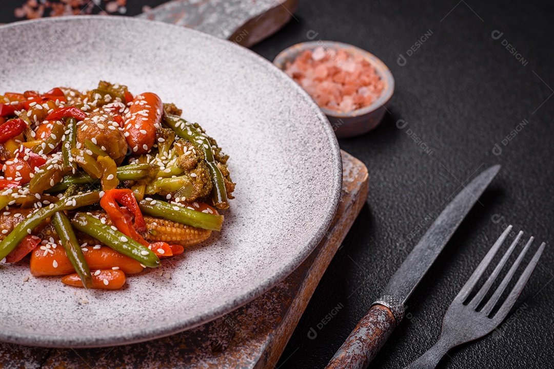Mistura de legumes, milho, cenoura, pimentão, brócolis, cebola em molho teriyaki em uma placa de cerâmica sobre um fundo escuro de concreto