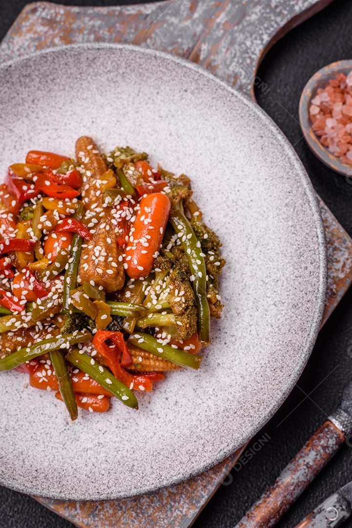 Mistura de legumes, milho, cenoura, pimentão, brócolis, cebola em molho teriyaki em uma placa de cerâmica sobre um fundo escuro de concreto
