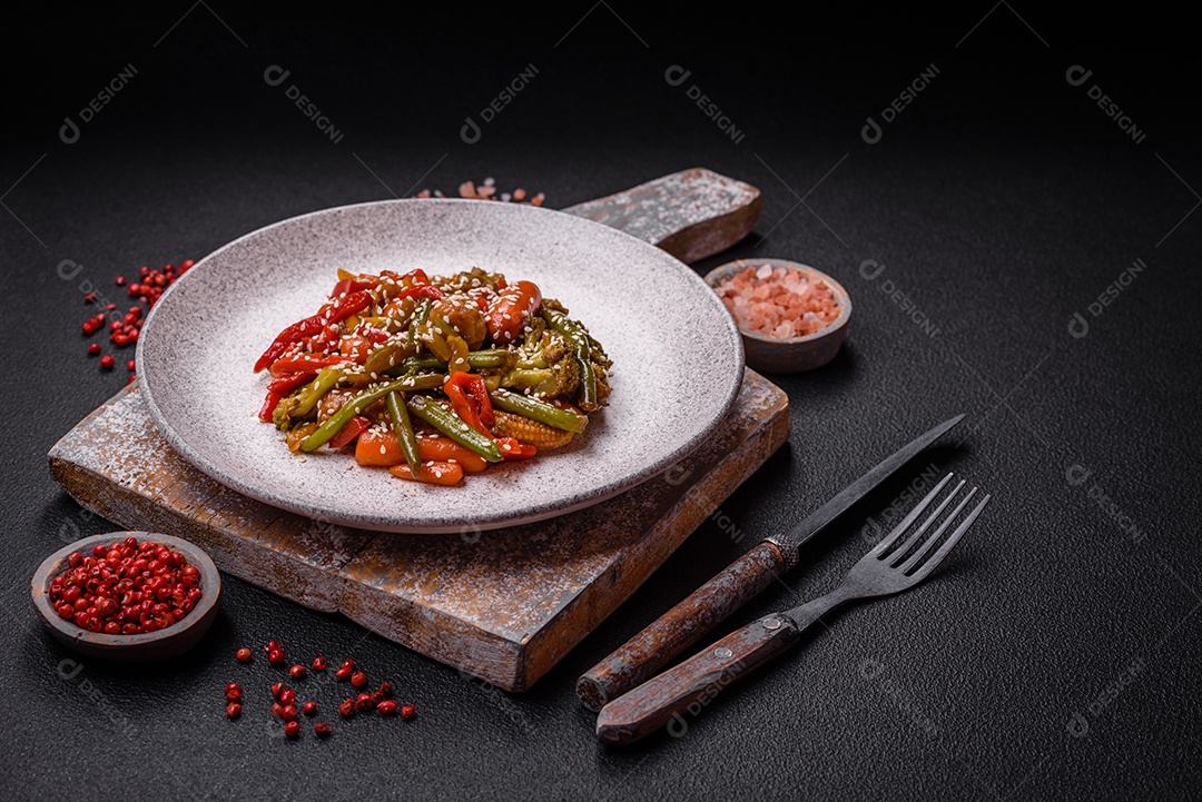 Mistura de legumes, milho, cenoura, pimentão, brócolis, cebola em molho teriyaki em uma placa de cerâmica sobre um fundo escuro de concreto