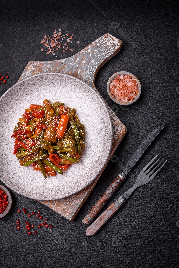 Mistura de legumes, milho, cenoura, pimentão, brócolis, cebola em molho teriyaki em uma placa de cerâmica sobre um fundo escuro de concreto