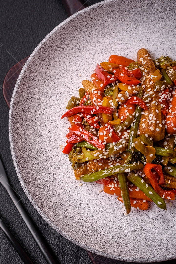 Mistura de legumes, milho, cenoura, pimentão, brócolis, cebola em molho teriyaki em uma placa de cerâmica sobre um fundo escuro de concreto