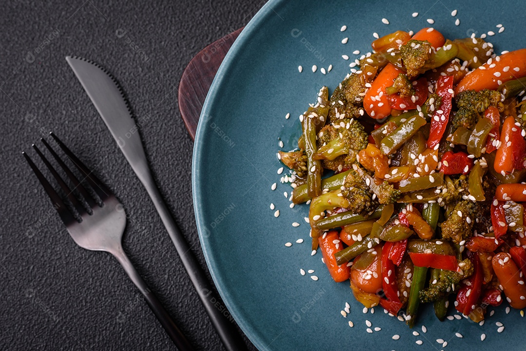 Mistura de legumes, milho, cenoura, pimentão, brócolis, cebola em molho teriyaki em uma placa de cerâmica sobre um fundo escuro de concreto