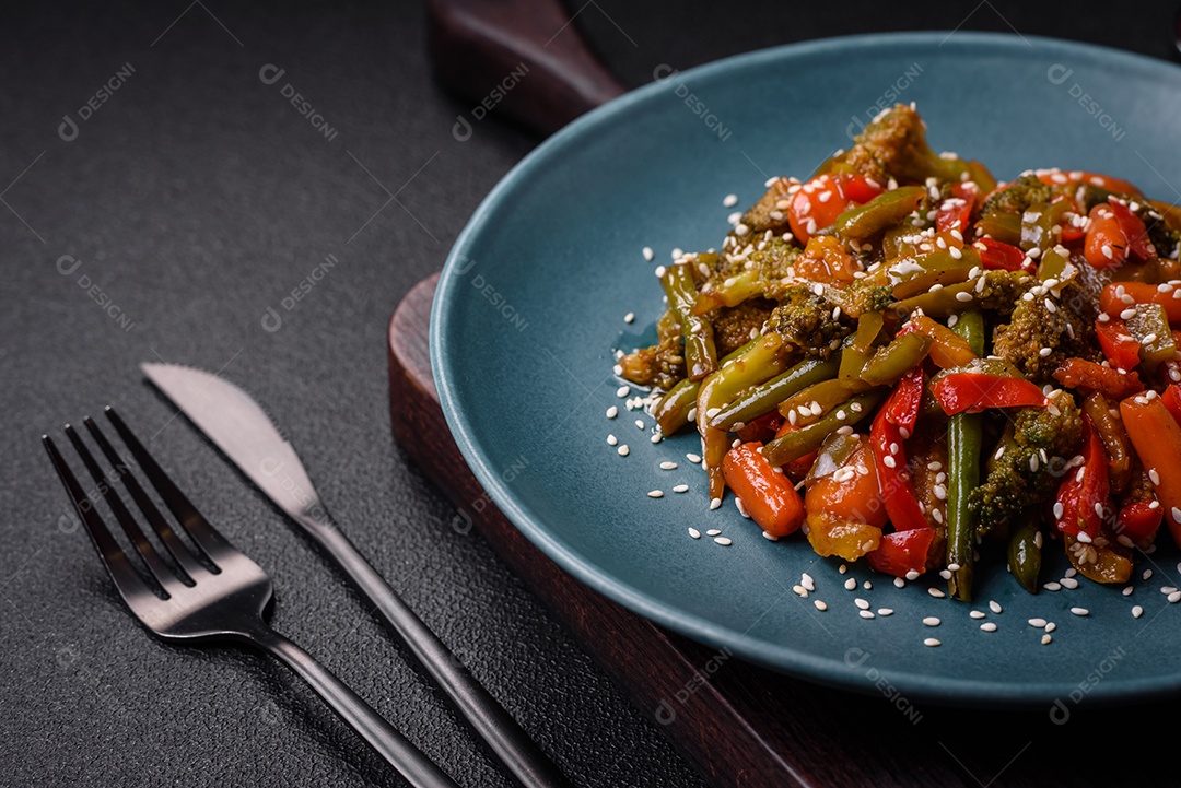 Mistura de legumes, milho, cenoura, pimentão, brócolis, cebola em molho teriyaki em uma placa de cerâmica sobre um fundo escuro de concreto