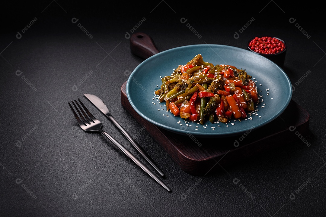 Mistura de legumes, milho, cenoura, pimentão, brócolis, cebola em molho teriyaki em uma placa de cerâmica sobre um fundo escuro de concreto