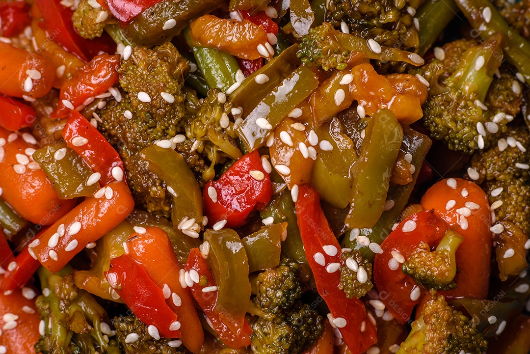 Mistura de legumes, milho, cenoura, pimentão, brócolis, cebola em molho teriyaki em uma placa de cerâmica sobre um fundo escuro de concreto