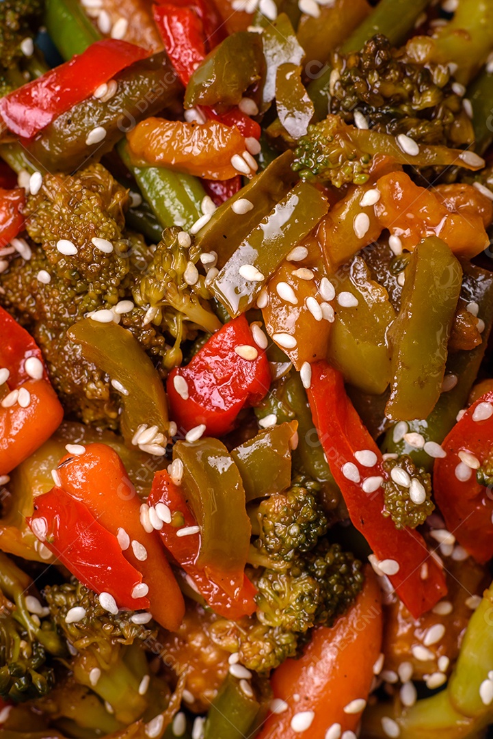 Mistura de legumes, milho, cenoura, pimentão, brócolis, cebola em molho teriyaki em uma placa de cerâmica sobre um fundo escuro de concreto