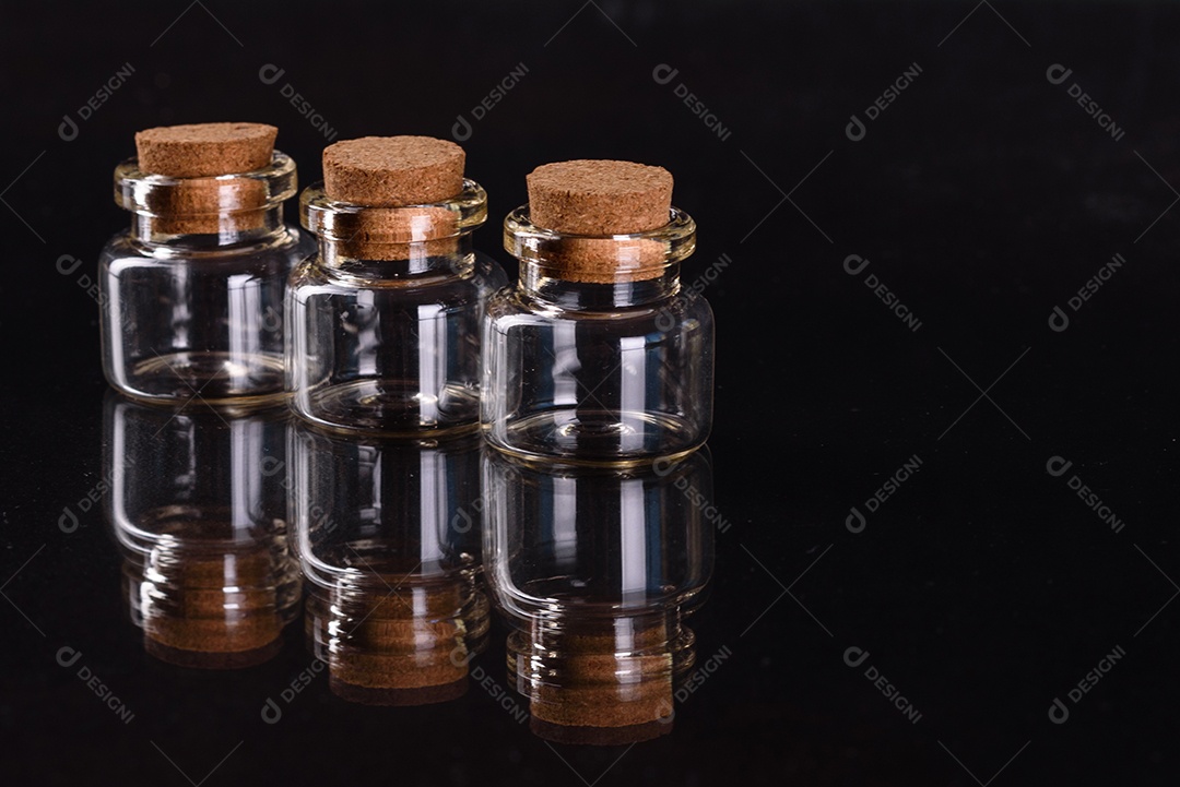 Conjunto de potes de vidro com rolhas de madeira cheias de diversas especiarias sobre um fundo escuro de concreto