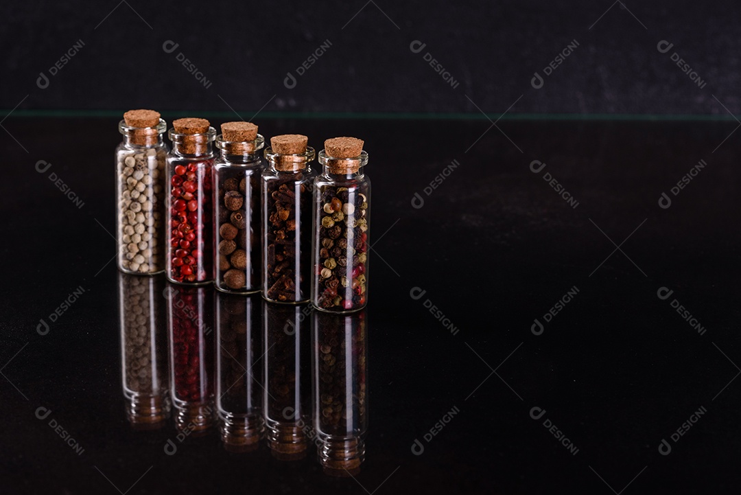 Conjunto de potes de vidro com rolhas de madeira cheias de diversas especiarias sobre um fundo escuro de concreto