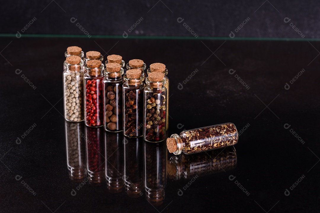Conjunto de potes de vidro com rolhas de madeira cheias de diversas especiarias sobre um fundo escuro de concreto