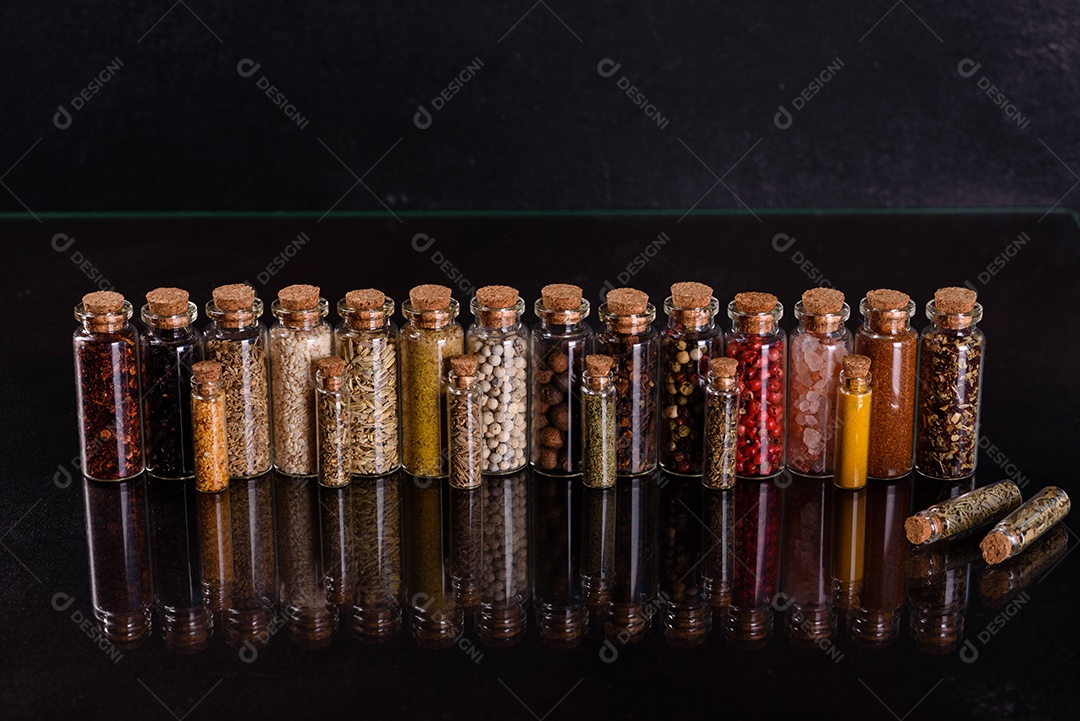 Conjunto de potes de vidro com rolhas de madeira cheias de diversas especiarias sobre um fundo escuro de concreto