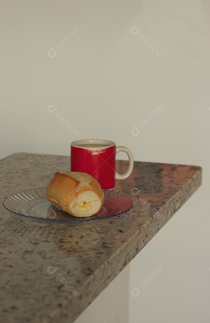 Xícara de café ao lado de pão francês sobre uma mesa