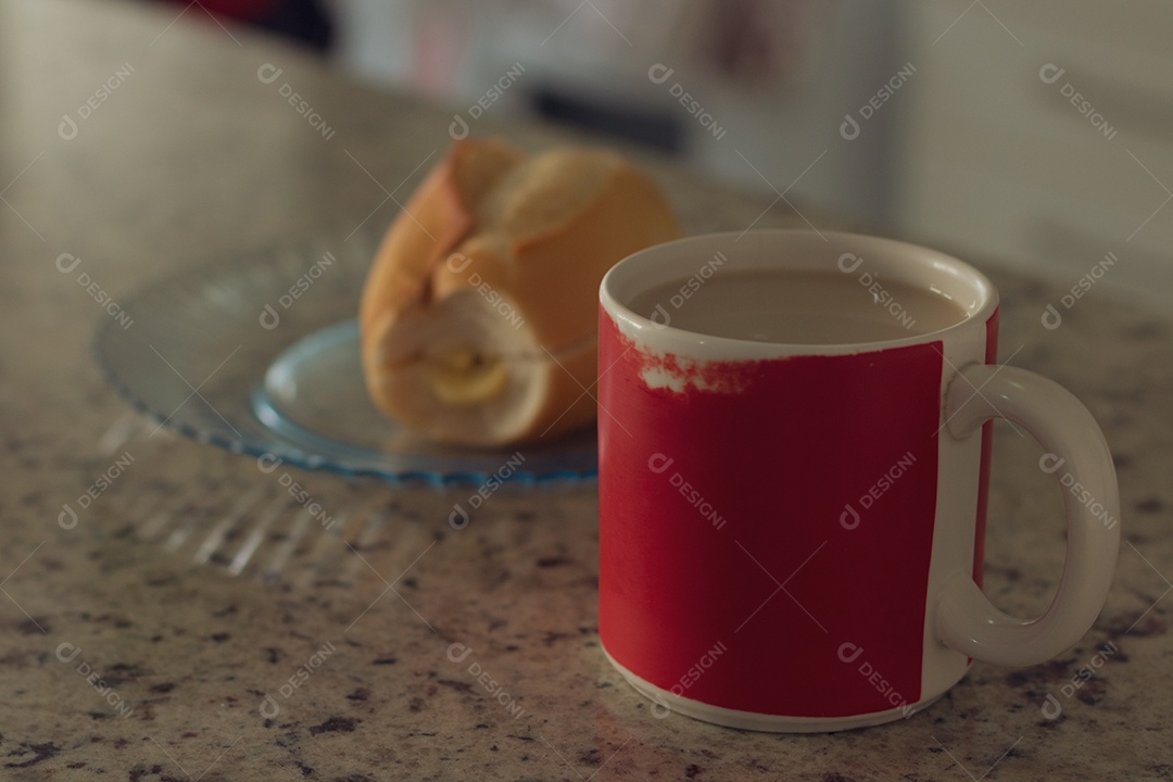 Xícara de café ao lado de pão francês sobre uma mesa