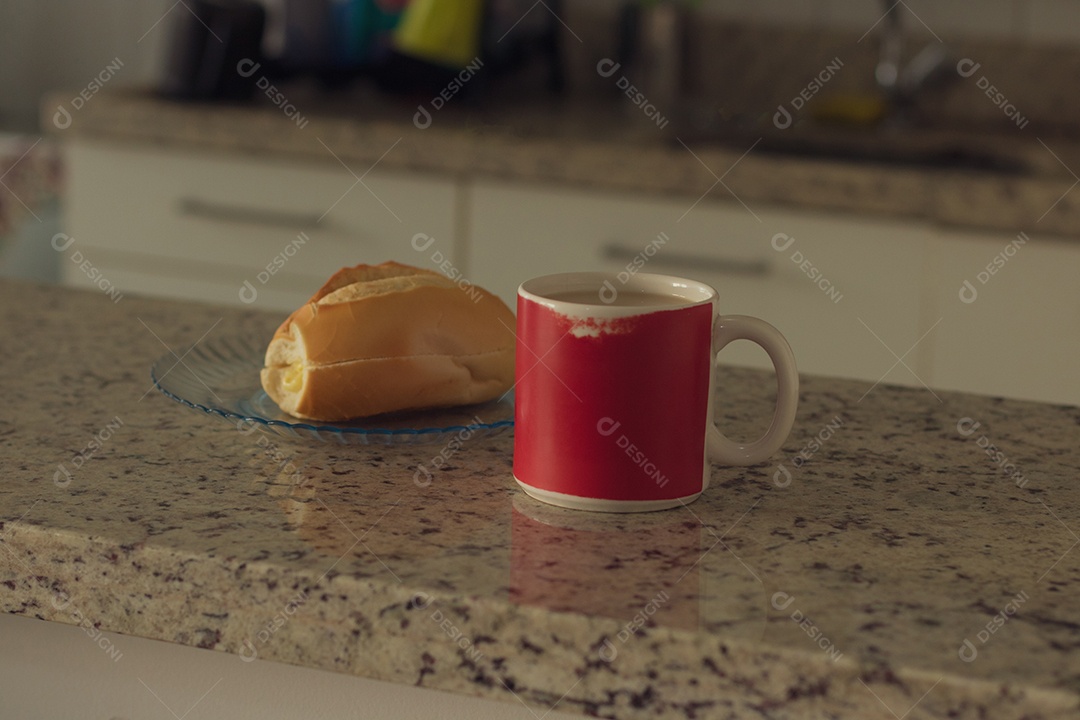 Xícara de café ao lado de pão francês sobre uma mesa