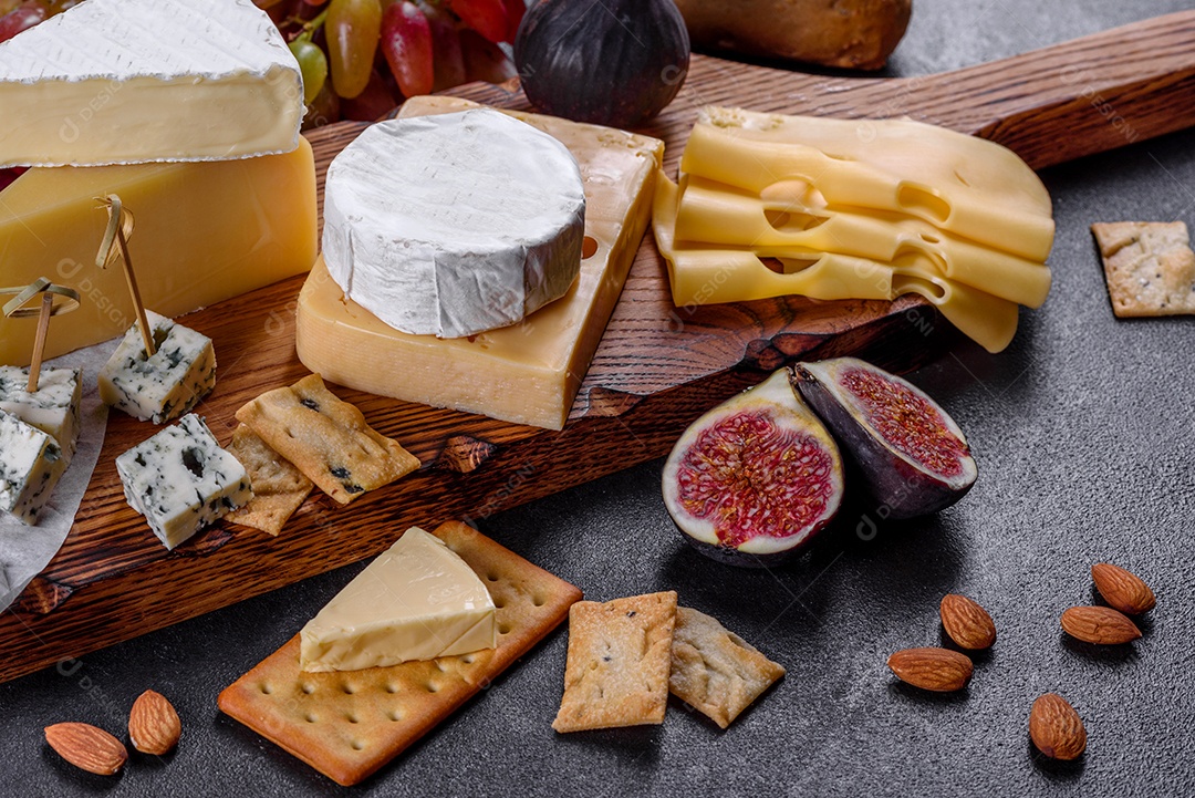 Lindo delicioso queijo camembert, parmesão, brie com uvas e figos em uma tábua de madeira.