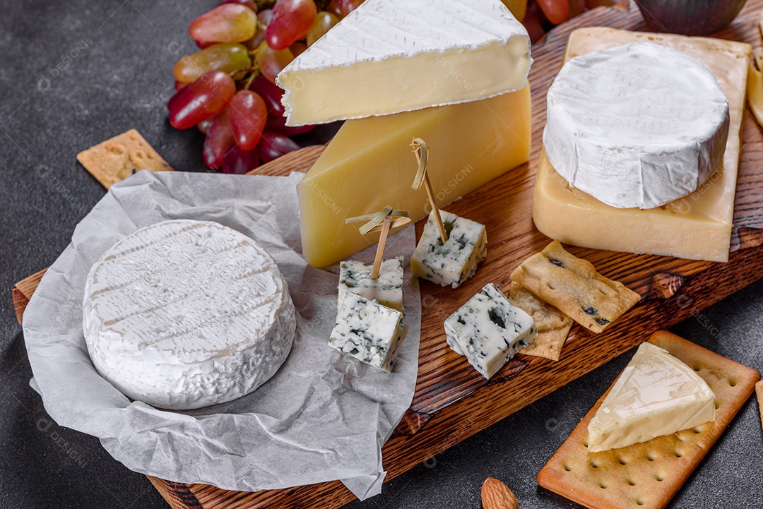 Lindo delicioso queijo camembert, parmesão, brie com uvas e figos em uma tábua de madeira.