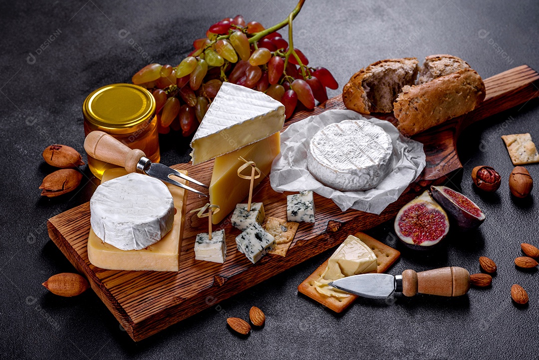 Lindo delicioso queijo camembert, parmesão, brie com uvas e figos em uma tábua de madeira.