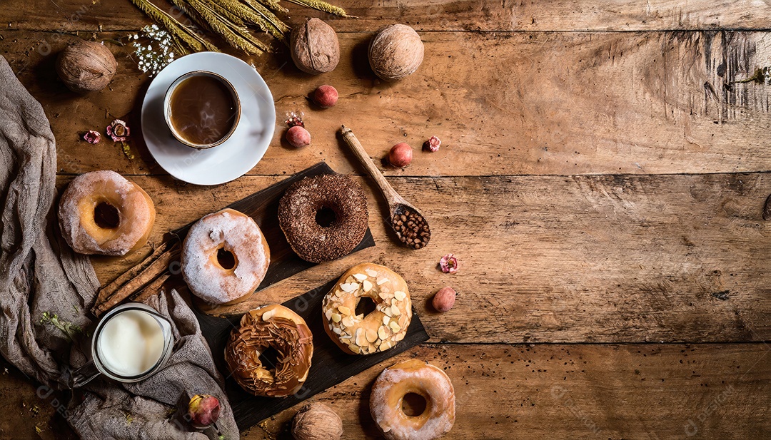 Variedade de donuts com granulado e glacê em fundo preto escuro de madeira