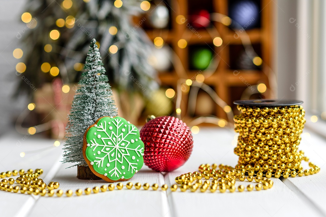 Lindas decorações de Natal multicoloridas sobre uma mesa de madeira clara com guirlandas e árvores de Natal ao fundo.
