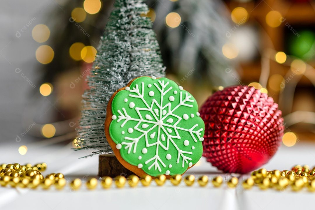 Lindas decorações de Natal multicoloridas sobre uma mesa de madeira clara com guirlandas e árvores de Natal ao fundo.