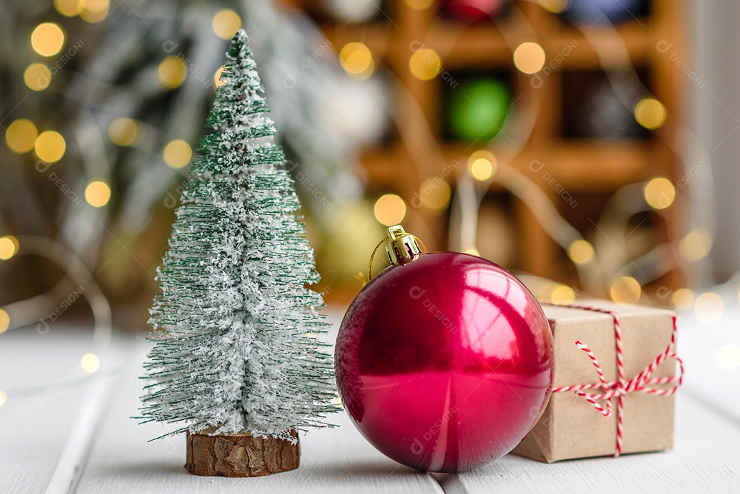 Lindas decorações de Natal multicoloridas sobre uma mesa de madeira clara com guirlandas e árvores de Natal ao fundo.