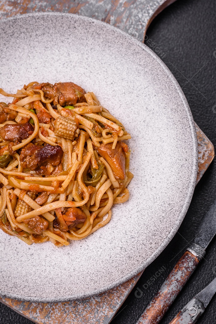 Delicioso prato de udon asiático com legumes, cogumelos, sal e especiarias numa placa cerâmica sobre um fundo escuro de concreto