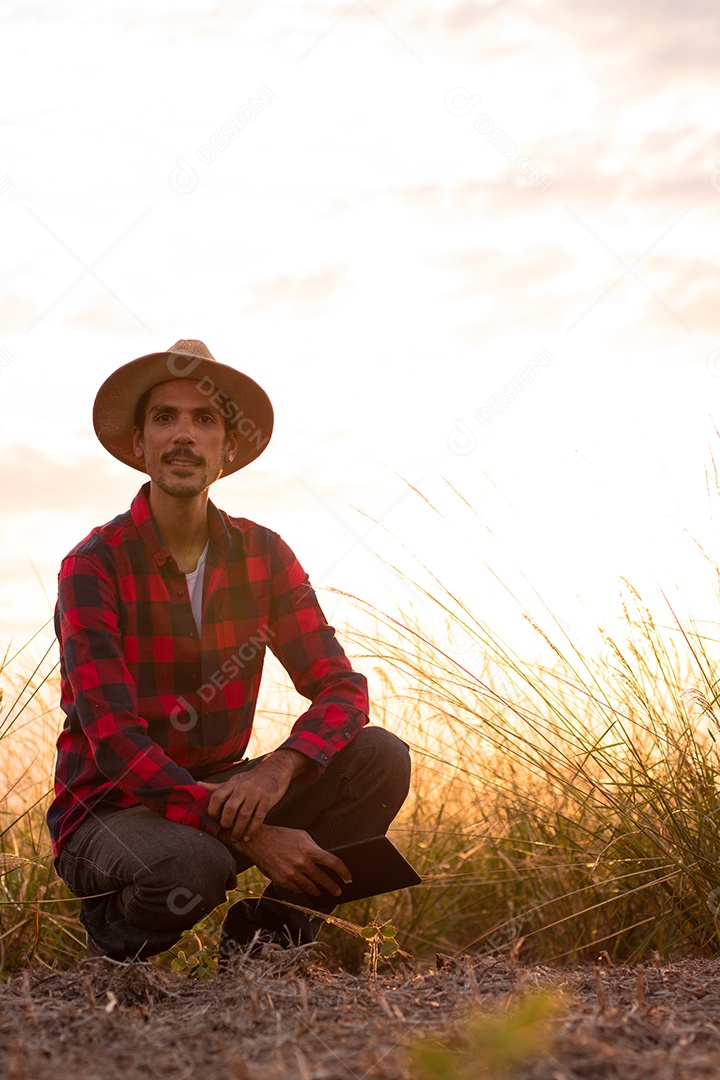 Agricultor com chapéu na plantação agrícola ao pôr do sol. Prédios e cidade desfocaram o fundo.
