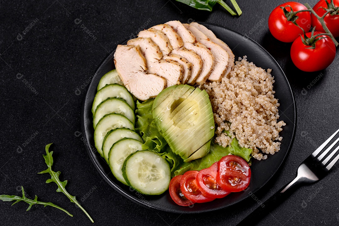 Salada deliciosa fresca com quinoa, frango e legumes frescos num prato sobre um fundo escuro de concreto