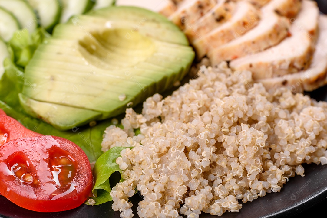 Salada deliciosa fresca com quinoa, frango e legumes frescos num prato sobre um fundo escuro de concreto