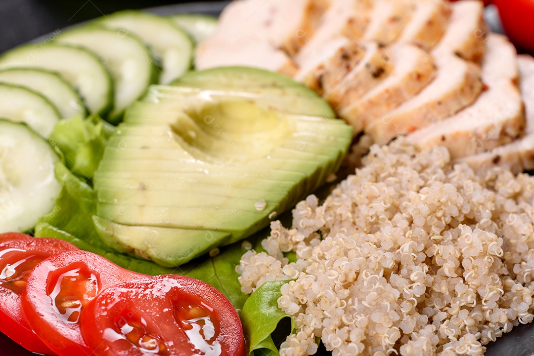 Salada deliciosa fresca com quinoa, frango e legumes frescos num prato sobre um fundo escuro de concreto