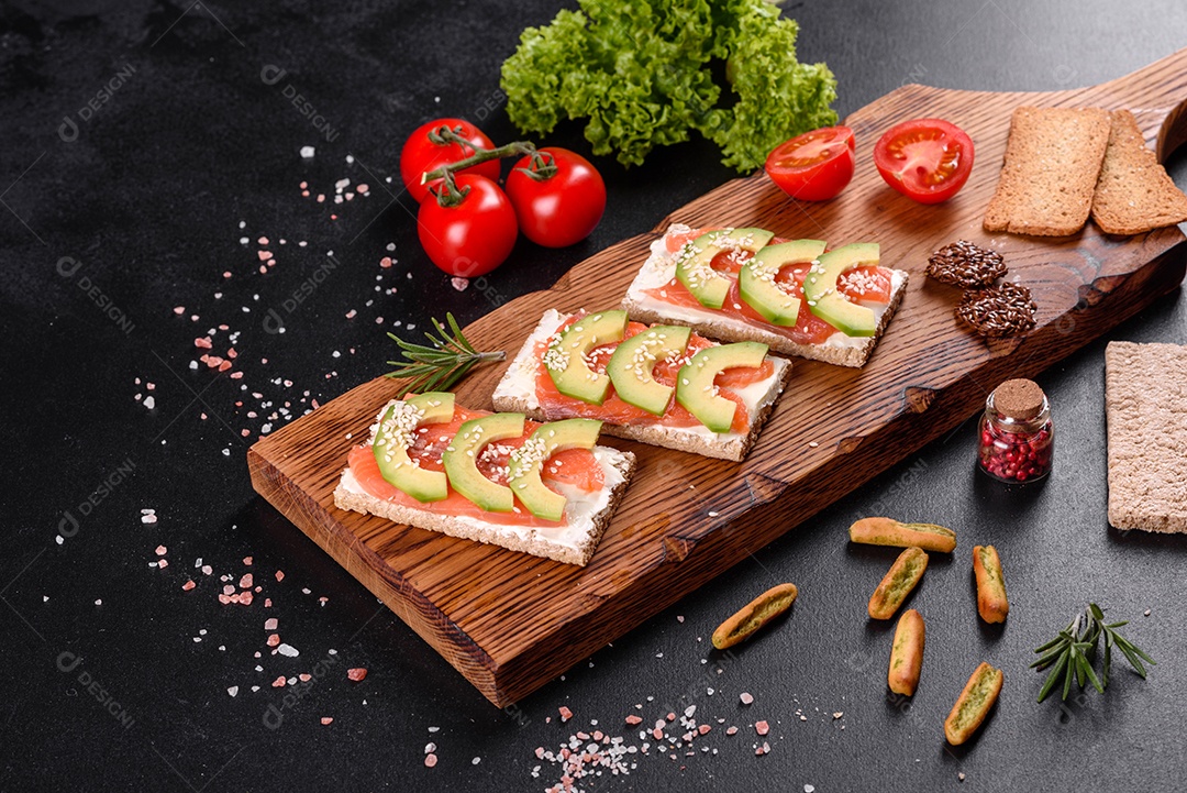 Delicioso sanduíche fresco com peixe vermelho, manteiga, pão e abacate em uma mesa de concreto escuro