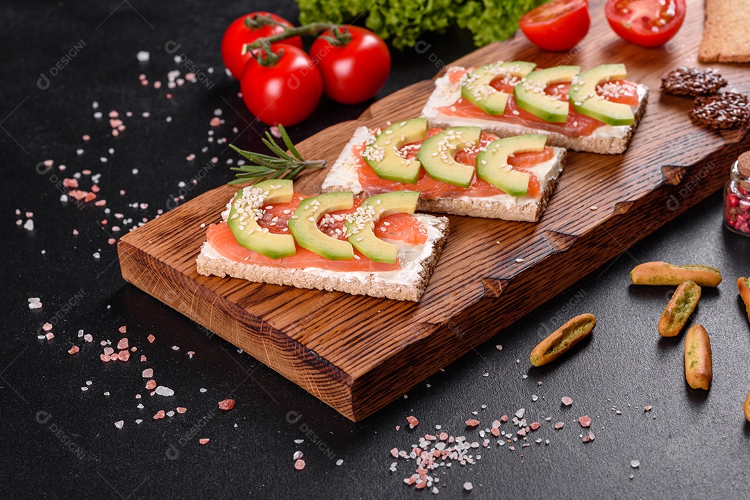 Delicioso sanduíche fresco com peixe vermelho, manteiga, pão e abacate em uma mesa de concreto escuro