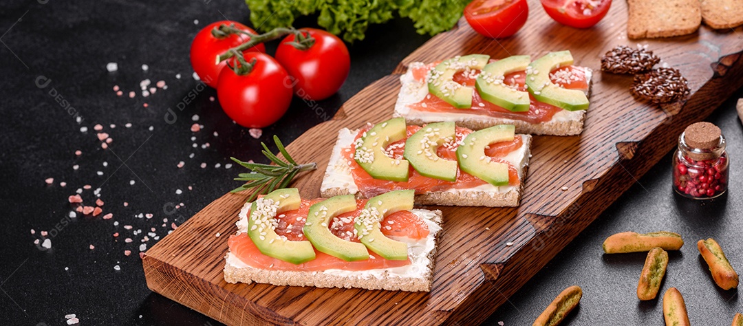 Delicioso sanduíche fresco com peixe vermelho, manteiga, pão e abacate em uma mesa de concreto escuro