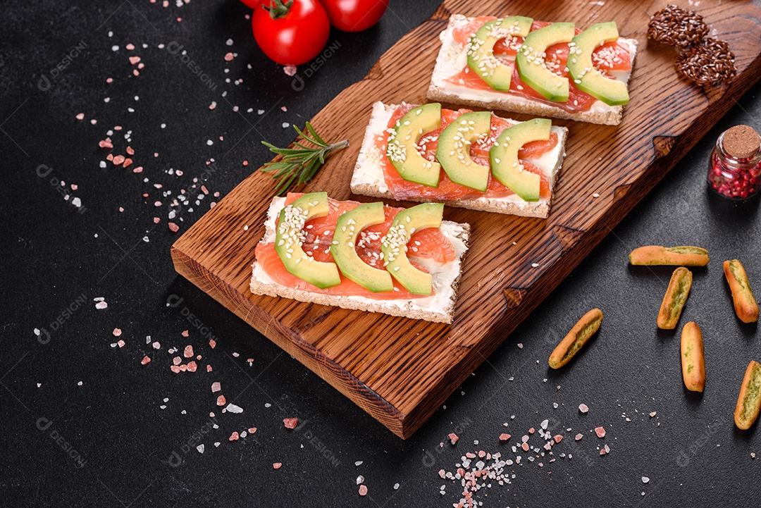 Delicioso sanduíche fresco com peixe vermelho, manteiga, pão e abacate em uma mesa de concreto escuro